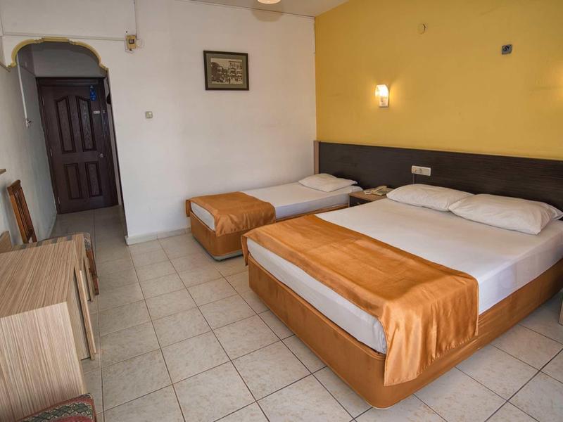 Jednoduchý hotelový pokoj s manželskou postelí, jednolůžkem, psacím stolem a televizí s plochou obrazovkou.