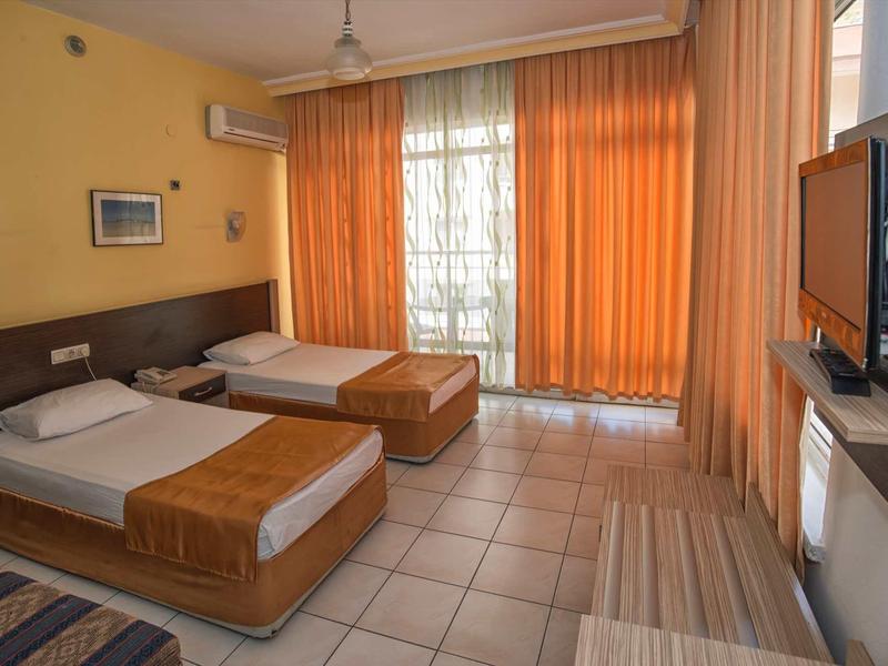 Jasný hotelový pokoj se dvěma jednolůžky, oranžovými závěsy a televizí.