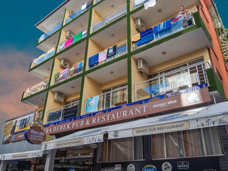 Vícepodlažní budova s balkony a restaurací v přízemí pod modrou oblohou