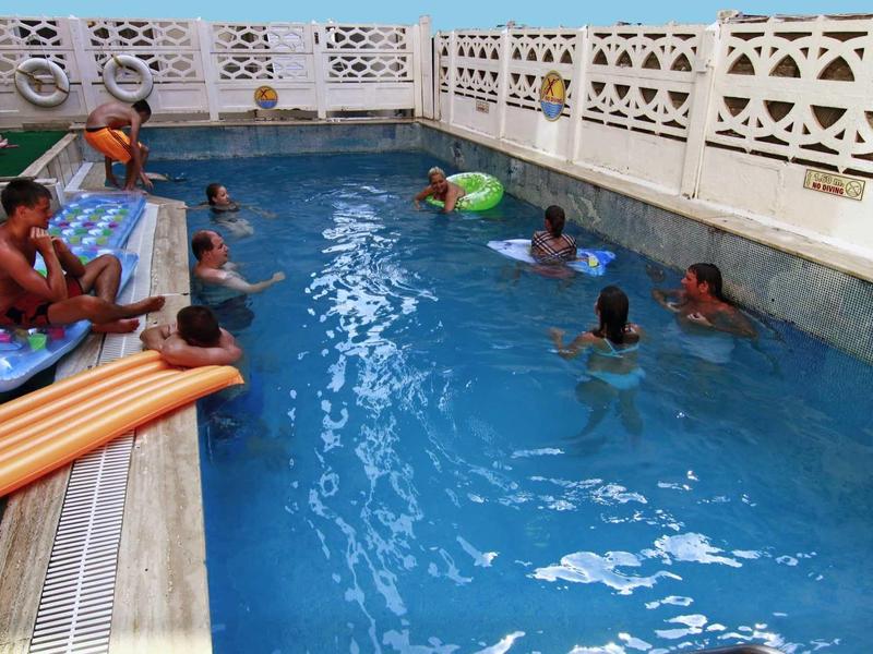 Děti plavou a hrají si v malém venkovním bazénu s bílým mřížkovým oplocením.