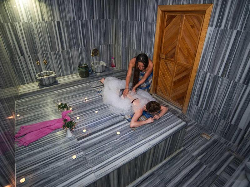 Žena dostává masáž v elegantní spa místnosti se šedým mramorem a světlem svící.