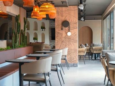 Modernes Café mit beigen Stühlen, Holztischen, Kakteen und warmen Pendelleuchten an der Decke.