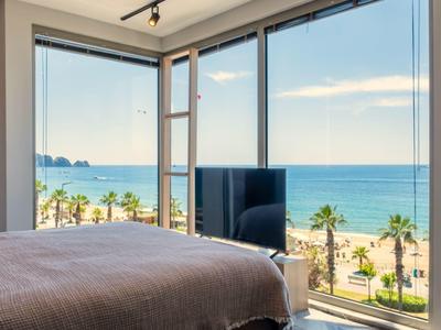 Helles Schlafzimmer mit Panoramafenster, Blick auf Meer, Strand und Palmen, modernes Design, Tageslicht.
