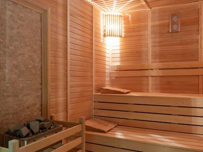 Holzsauna mit Holzbänken, Saunaofen mit Steinen und warmem Licht an der Wand.