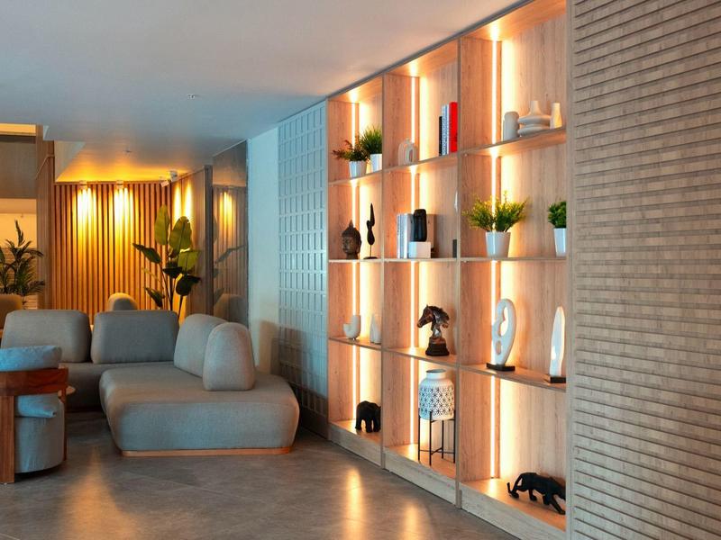 Modernes Wohnzimmer mit grauem Sofa, bunten Hockern und beleuchtetem Wandregal aus Holz.