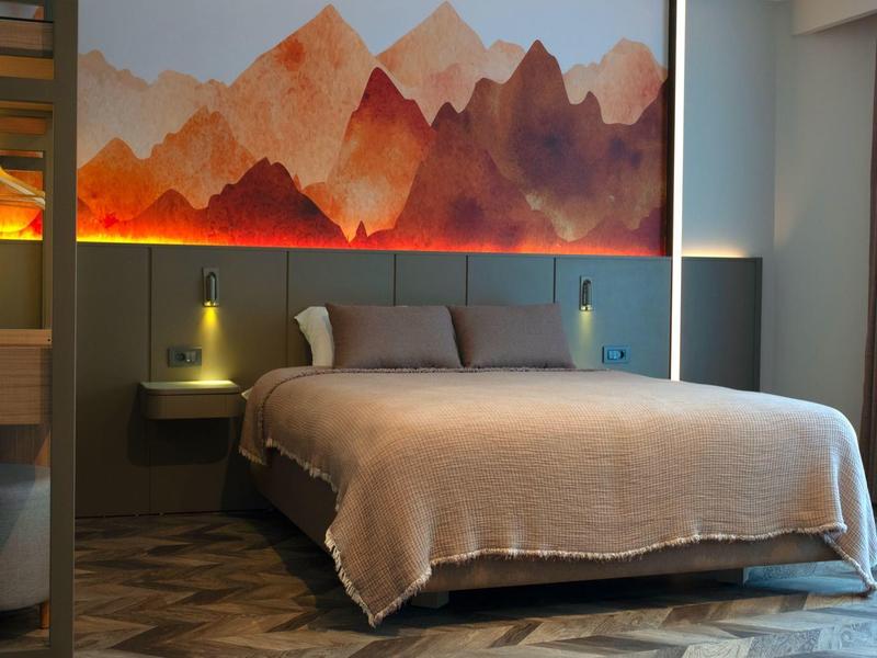 Modernes Schlafzimmer mit großem Bett, Berglandschaft-Wandbild und gedimmter Beleuchtung.