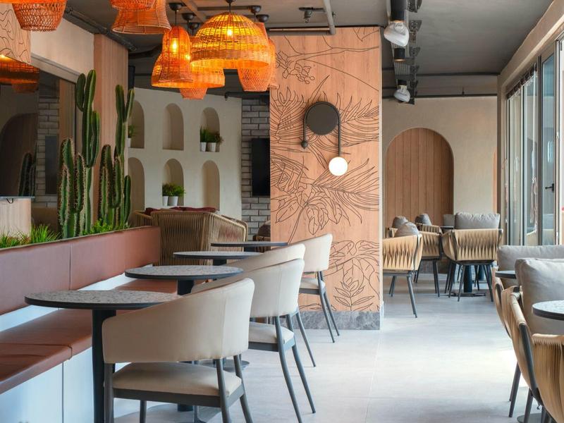 Modernes Café mit beigen Stühlen, Holztischen, Kakteen und warmen Pendelleuchten an der Decke.