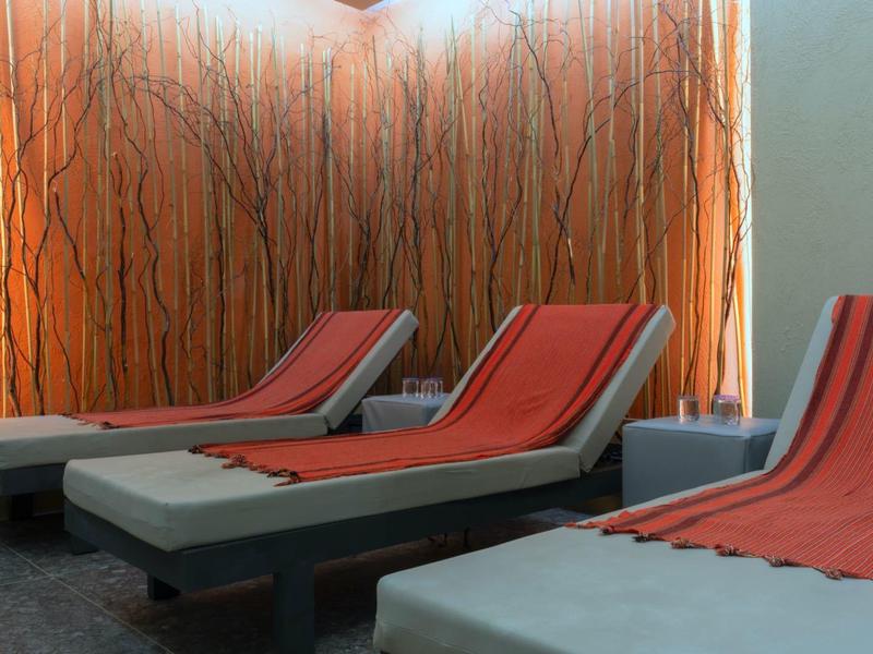 Drei Liegestühle mit roten Polstern vor Wand mit braunen Zweigdekorationen und warmem Licht.