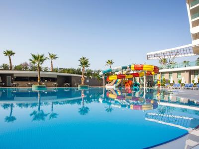 Großer Hotelpool mit Wasserrutschen, Liegestühlen und Palmen unter blauem Himmel.