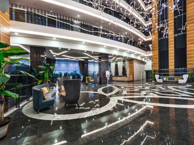 Große moderne Lobby mit glänzendem Marmorboden, Pflanzen, Sitzgruppen und beleuchtetem Deckendekor.