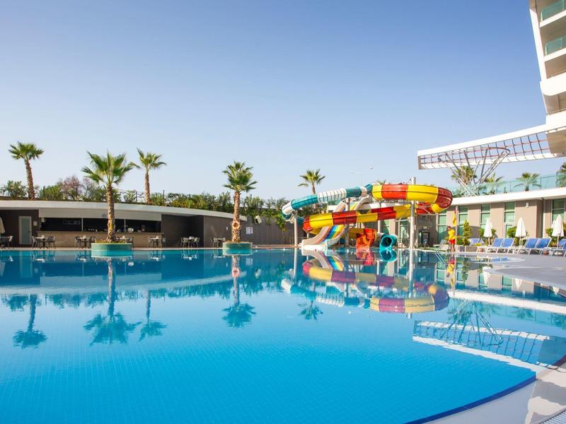 Gran piscina del hotel con toboganes acuáticos coloridos y palmeras bajo un cielo claro.