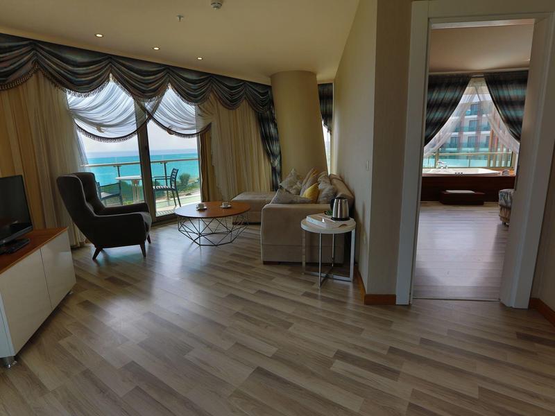 Habitación de hotel luminosa con vista al mar, área de estar y dormitorio contiguo.