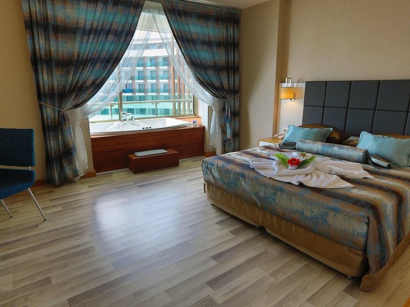 Habitat luminoso con cama grande, ventana con cortinas y silla junto a la cama.