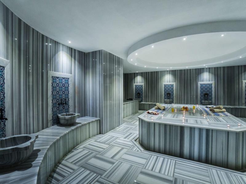Hammam elegante con piscinas de mármol, área de lavado central y iluminación suave.