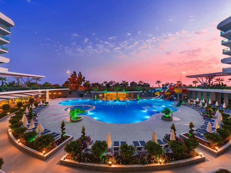 Una piscina redonda de hotel al atardecer con tumbonas y plantas verdes.
