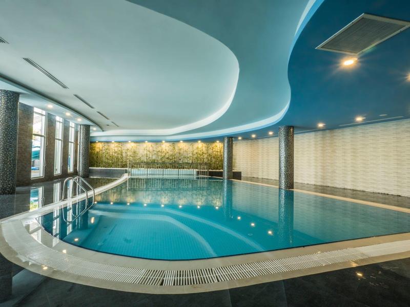 Piscina interior moderna con iluminación indirecta y techo azul en un hotel.