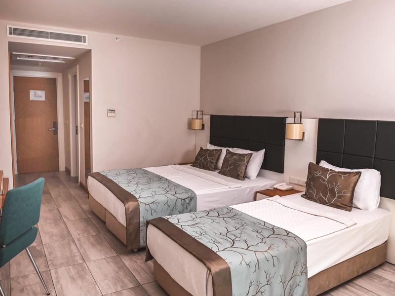 Habitación de hotel con dos camas sencillas, muebles de madera modernos y iluminación amable.