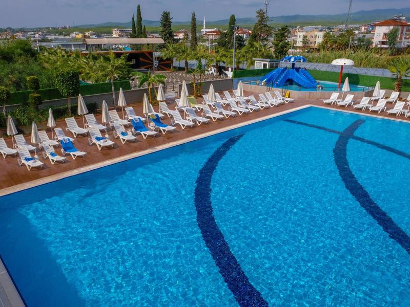 Gran piscina exterior clara con tumbonas y tobogán de agua en un entorno soleado.