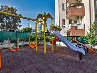 Aire de jeux pour enfants avec balançoires colorées et toboggan bleu à côté d'un immeuble résidentiel.