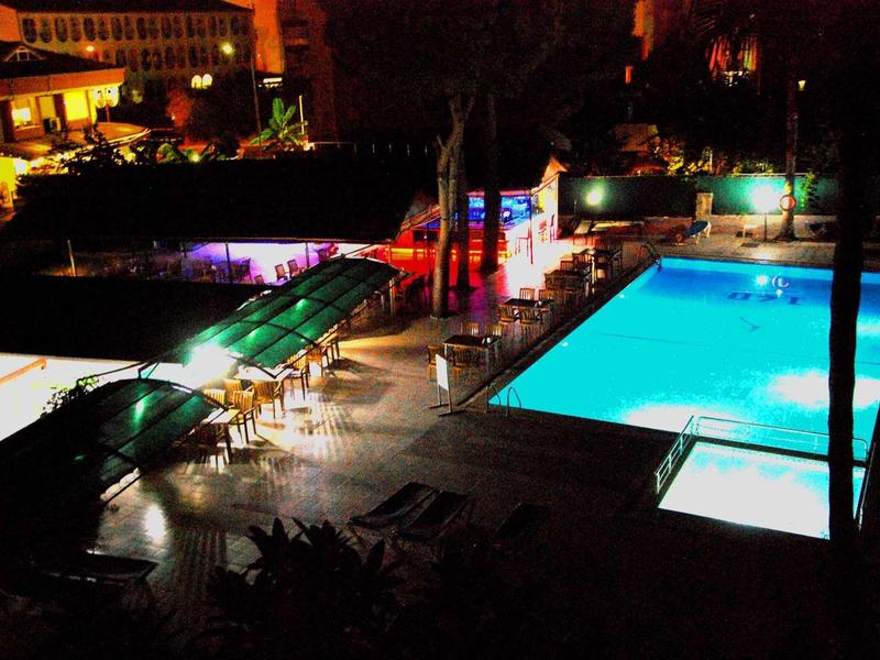 Zone de piscine d'hôtel éclairée avec chaises longues la nuit.