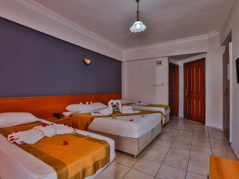 Chambre d'hôtel avec trois lits simples, télévision à écran plat et sol carrelé.