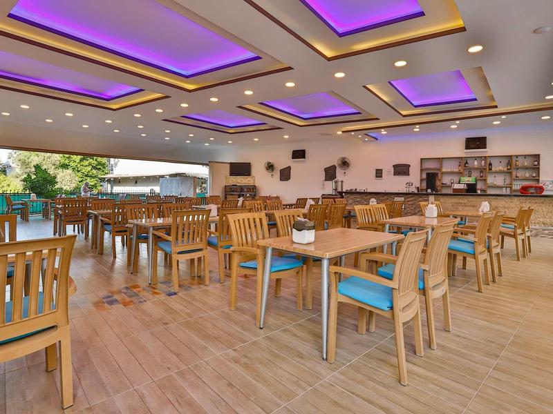 Grande salle à manger avec des chaises en bois et des coussins bleus, éclairée par des lumières violettes au plafond.