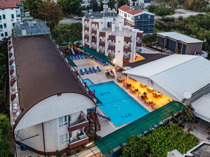 Complexe hôtelier avec piscines, terrasse ensoleillée et bâtiments à plusieurs étages dans une zone boisée.