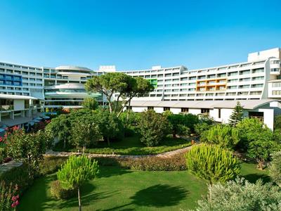 Großes weißes Hotelgebäude mit mehreren Stockwerken und großem grünen Garten im Vordergrund.