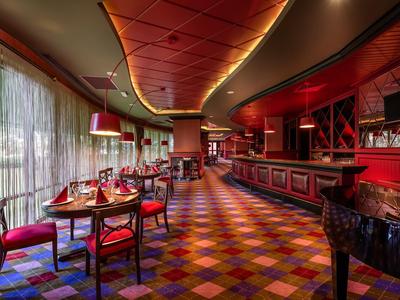 Elegantes Restaurant mit roter Inneneinrichtung und bunt gefliestem Boden, großem Fenster und gedämpftem Licht.