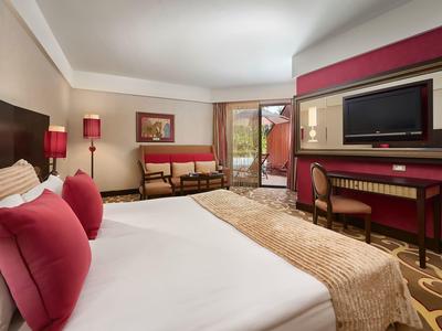 Modernes Hotelzimmer mit großem Bett, TV, Schreibtisch und Zugang zu einem Balkon.