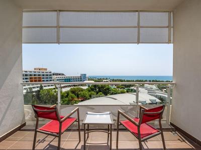 Balkon mit zwei roten Stühlen und kleinem Tisch mit Meerblick und Gebäuden im Hintergrund.