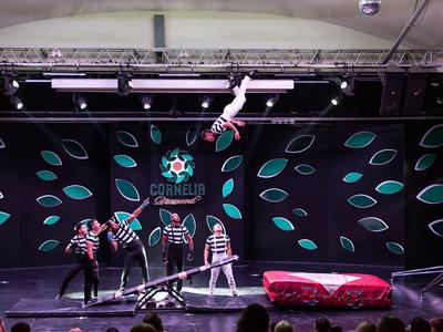 Artysta cyrkowy balansujący na linie, czterech pomocników poniżej na oświetlonej scenie.