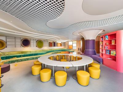 Bunte, moderne Kinderbibliothek mit runden Sitzgruppen, gelben Hockern und bunten Regalen.