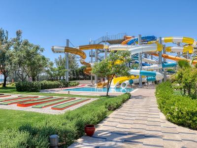 Wasserpark mit bunten Rutschen, Spazierweg und grünen Pflanzen unter klarem Himmel.