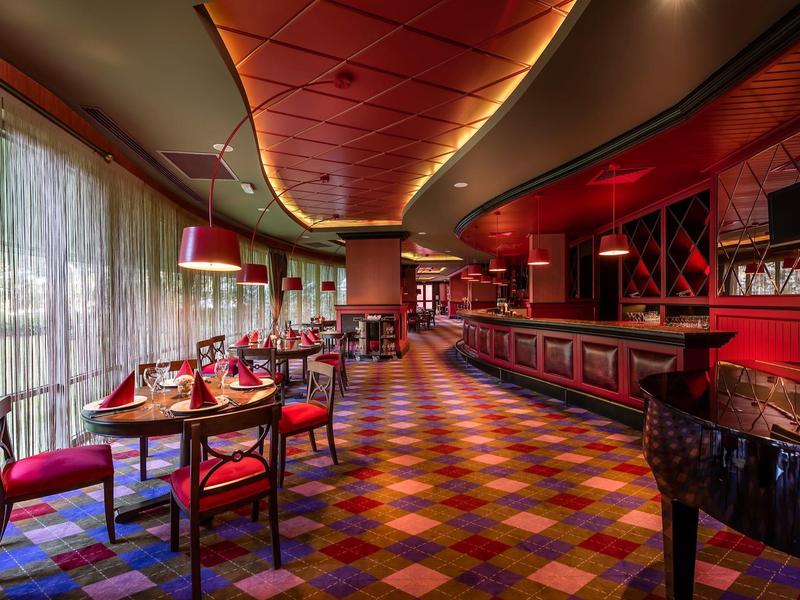 Elegantes Restaurant mit roter Inneneinrichtung und bunt gefliestem Boden, großem Fenster und gedämpftem Licht.