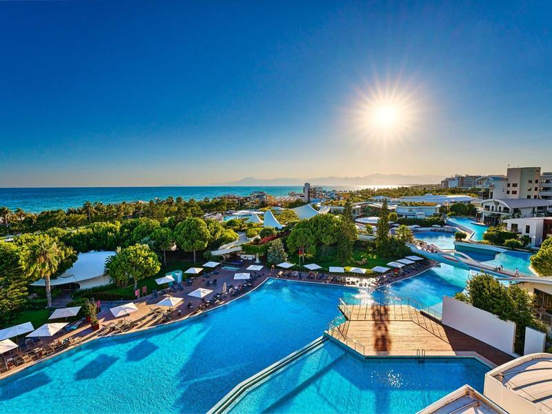 Großer Hotelpool mit Liegestühlen und Blick auf Meer unter hellem Sonnenschein.