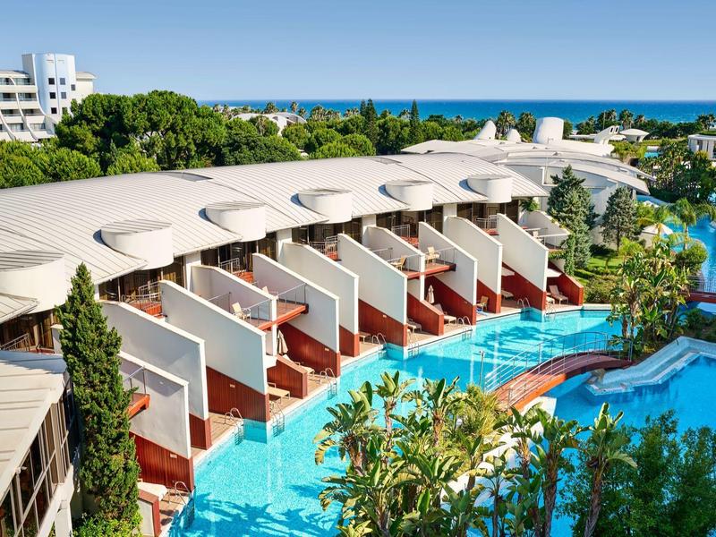 Moderne Hotelanlage mit Pool, mehrstöckigen Zimmern und Meerblick im Hintergrund.