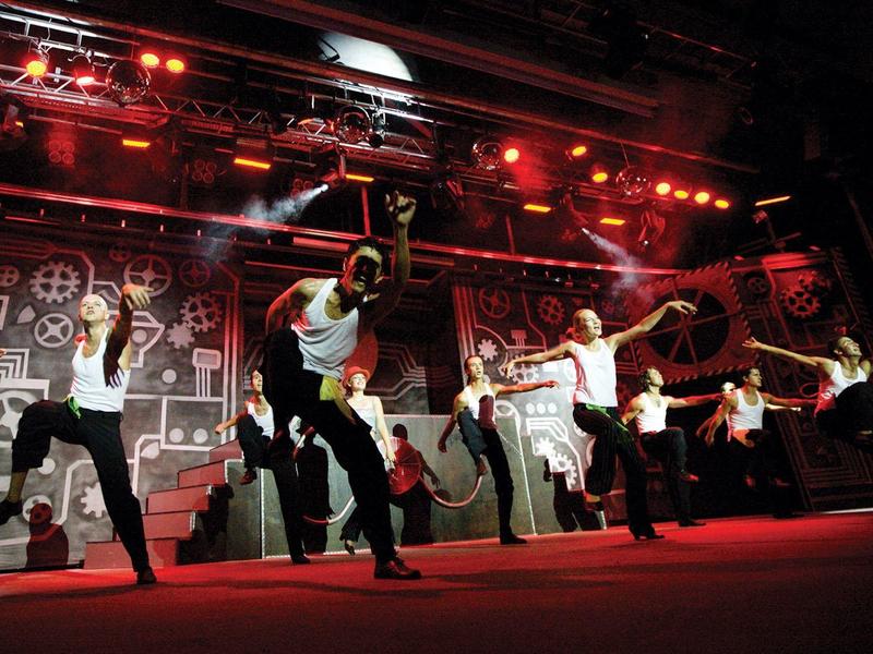 Tanzgruppe führt eine energiegeladene Performance auf einer Bühne mit roter Beleuchtung auf.