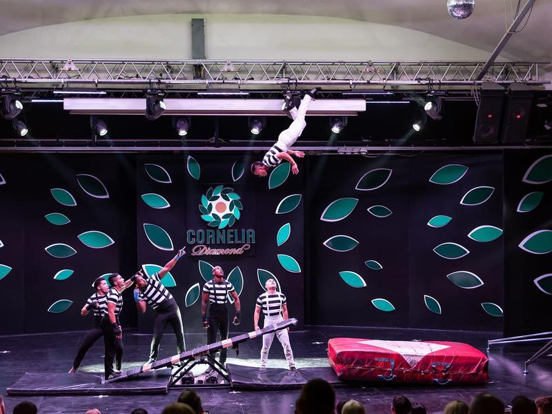 Eine Akrobatikshow mit einer Person, die kopfüber an einem Seil hängt, während andere Performer darunter stehen.