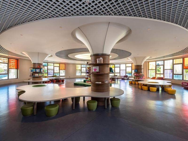 Großer runder Gemeinschaftsraum mit bunten Stühlen und geschwungenen Tischen in einem Hotel.