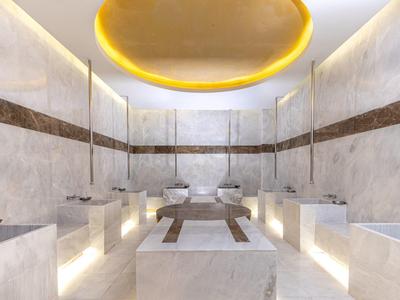 Sala de bienestar moderna con bancos de piedra y duchas de vapor, iluminación cálida indirecta.