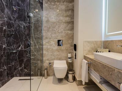 Baño moderno con ducha walk-in, inodoro de pared y gran espejo iluminado.