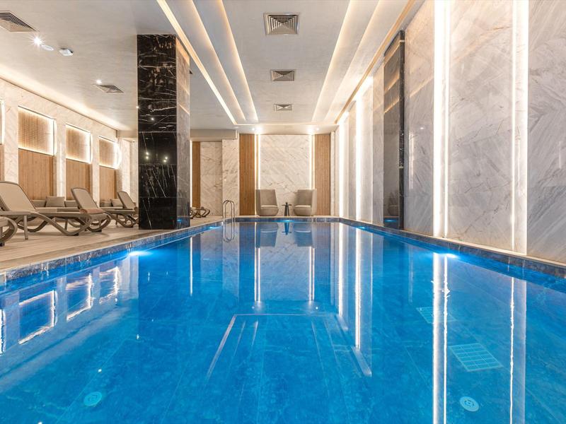 Piscina interior moderna con tumbonas y luz cálida para días de vacaciones relajantes.