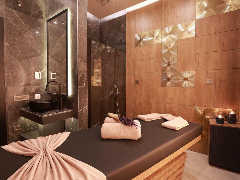 Sala de masajes cálida con paredes de madera, camilla oscura, toallas e iluminación ambiental.