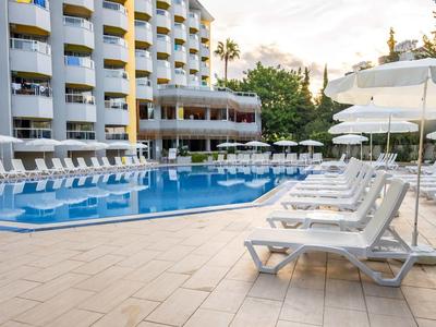 Empty hotel pool area with white lounge chairs under umbrellas and multiple balconies.
