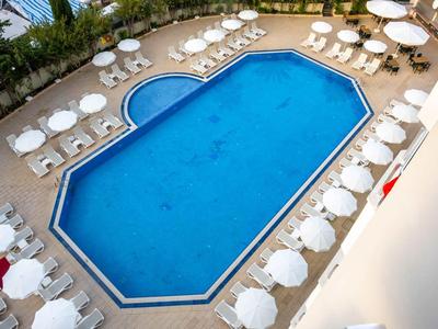 Rectangular outdoor pool surrounded by white lounge chairs and umbrellas.