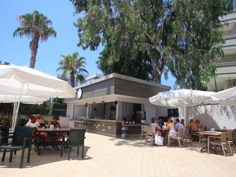 Outdoor café with umbrellas and guests in a sunny hotel setting with palm trees.