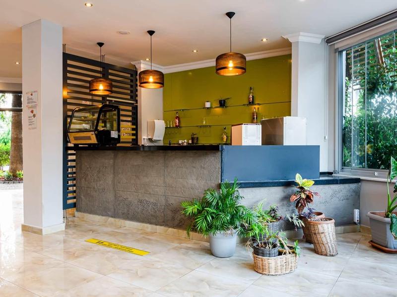 Modern hotel reception with green accents, plants, and warm hanging lamps.