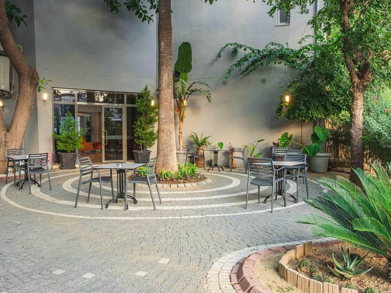 Outdoor café area with multiple tables and chairs in a green courtyard.