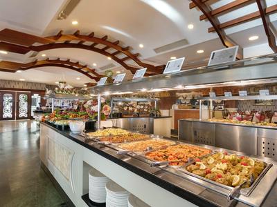 Buffet mit verschiedenen warmen Speisen, helle Decke mit Holzverzierungen und großes, offenes Restaurant.